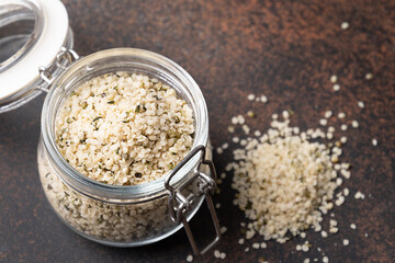 Healthy hemp kernels in glass jar on brown. Close up