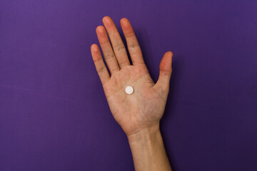 Hand holding a pill on a purple background.