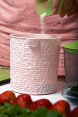A woman pours sugar into a container for making dough. For the preparation of biscuit roll with spinach and mint. Stuffed with strawberries. Ingredients for cooking.