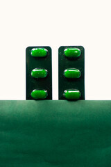 Pills in packaging on green and white background.