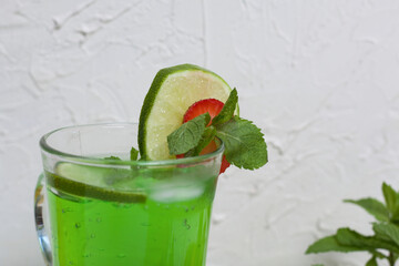 Green lemonade in a glass. Decorated with lime and strawberries. With sprigs of mint.