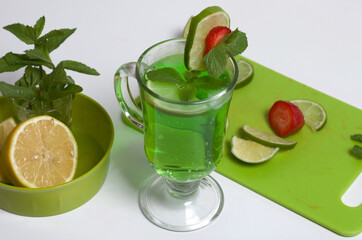 Green lemonade in a glass. Decorated with lime and strawberries. With sprigs of mint. Near lemon and mint.