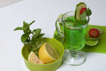Green lemonade in a glass. Decorated with lime and strawberries. With sprigs of mint. Near lemon and mint.