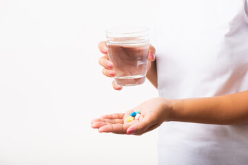 Closeup young Asian woman hold pill drugs in hand ready take medicines with a glass of water, studio shot isolated on white background, Healthcare and medical pharmacy concept