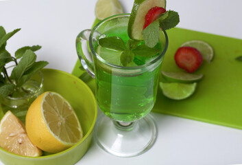 Green lemonade in a glass. Decorated with lime and strawberries. With sprigs of mint. Near lemon and mint.
