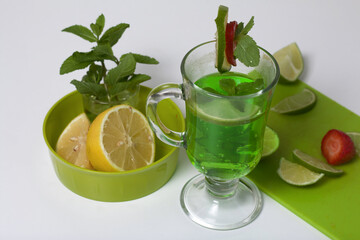 Green lemonade in a glass. Decorated with lime and strawberries. With sprigs of mint. Near lemon and mint.