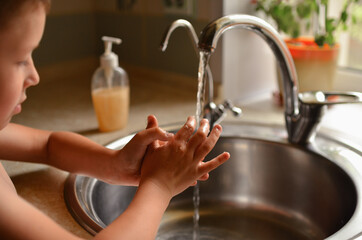 The child washes his hands in the house. Water tap for washing hands.