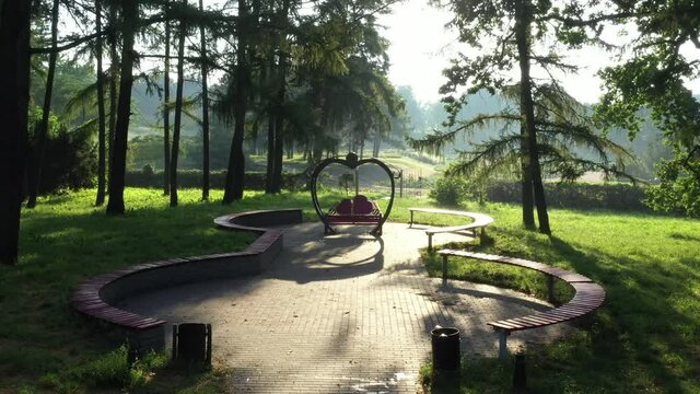 Gazebo Arbor Altanka for lovers: a bench under the roof with two hearts. Zoom Out Crane Shot. Arbor of lovers in the park among the trees in the summer. Distant plan.