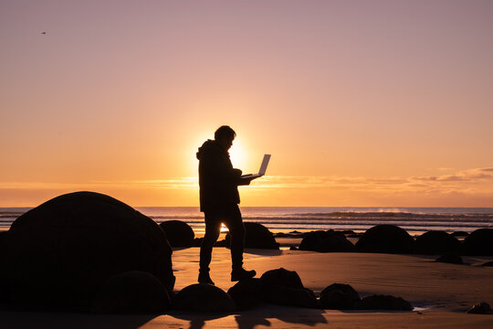 Asian Man Traveller Visit At Moereki Boulder, New Zealand. Frelancer Remotely Worker.