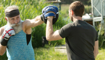 Fototapeta premium Older man boxing outdoor. Senior man with personal trainer.