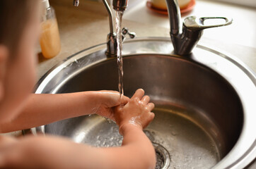 The child washes his hands in the house. Water tap for washing hands.