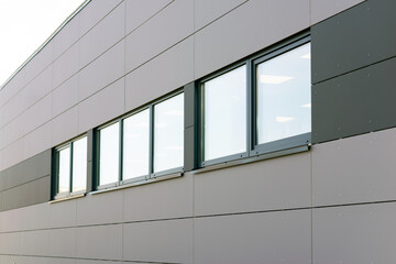 Details of gray facade with windows on industrial building reflect clouds on windows