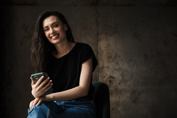 Photo of beautiful smiling woman sitting on chair and holding cellphone