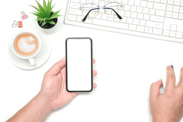 Flat lay, Workspace business office and education concept on white table desk with hand holding blank screen phone and mouse, Keyboard and green, coffee cup and paper clip, Top view  with copy space