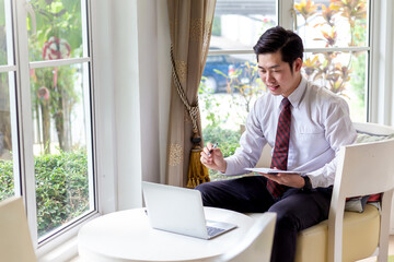 Portrait of young asian businessman sitting and thinking and analyzing document with laptop in the office.