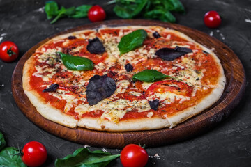 Perfect pizza margarita with tomato slices, basil and cherry tomatoes on a dark background.