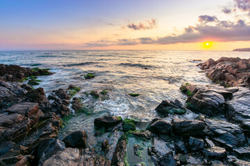 coast of the ocean at sunset. beautiful landscape with rocks in the water. gorgeous cloudscape above the sun and horizon. concept of calmness and mediatation