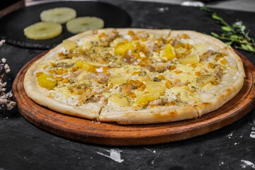 Isolated Pizza with chicken and pineapple on a wooden board, and on a dark background