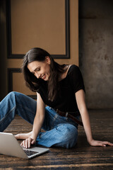 Photo of beautiful young woman sitting on floor and using laptop