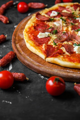 Meat pizza with salami, ham, chicken, sausages and feta cheese, on a blackboard and on a dark background