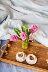 Obraz na płótnie Canvas A bouquet of beautiful pink hyacinths stands in a vase on a tray, two cups of cappuccino with a heart pattern, the concept of a surprise in bed. Place for an inscription. Close-up