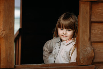 Little cute girl sits in the window of a wooden house
