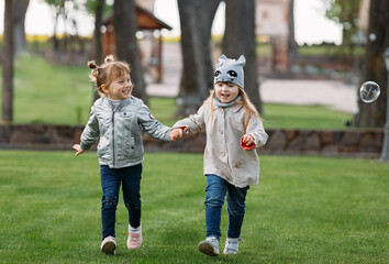 Two happy little sisters running in the park holding hands
