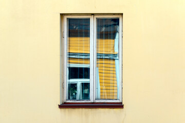 Fototapeta na wymiar Detail of traditional east european yellow building in a middle window reflection buildings in the sunny day