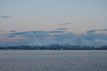 majestic snowy mountain with colourful sunset sky and beautiful cloud formation with cold fjord water underneath in wintertime