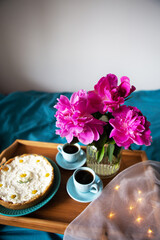 Beautiful morning Vanilla cheesecake, coffee, blue cups, pink peonies in a glass vase.