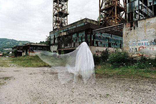 White transparent ghost near old abandoned mine building with rusty metal construction and shabby walls