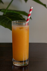 glass of orange juice with paper straw and ice on a wooden table