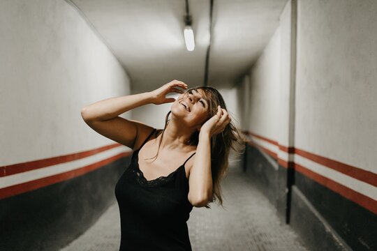 Young female in elegant black dress standing in enclosed underground passage and looking up dreamfully