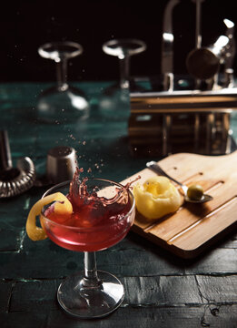 From above of red alcohol cocktail with splashes served in coupe glass garnished with lemon on bar counter