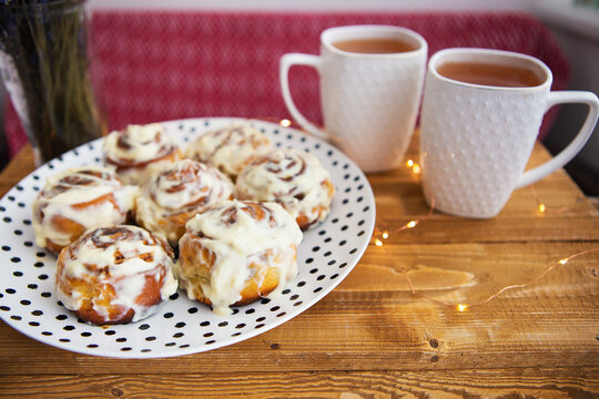 Two cups of black tea stand on a wooden tray, a bouquet of dried lavender. Fresh and fragrant cinnamon rolls close up lie on a plate with polka dots, beautiful morning. Close-up