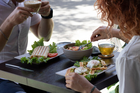 Couple eating lunch, breakfast or brunch outside the cafe, salad, tea, wrap, waffles, pouched eggs