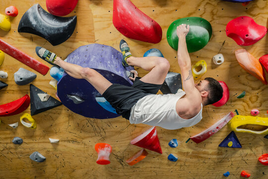 Side view of strong man in sportswear climbing high on colorful grips of wall during hard training in gym