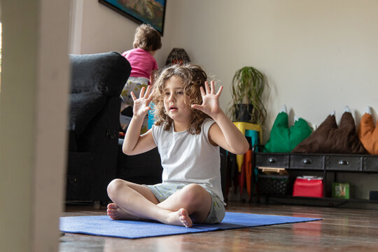 Side view of a little girl watching online video tutorial on laptop while sitting on mat and learning yoga pose at home
