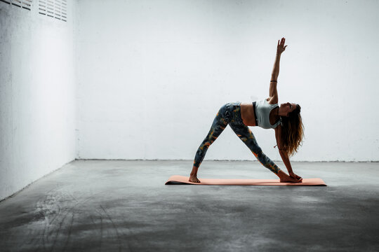 Side view of calm female wearing sports leggings and bra standing on mat in extended triangle pose looking up