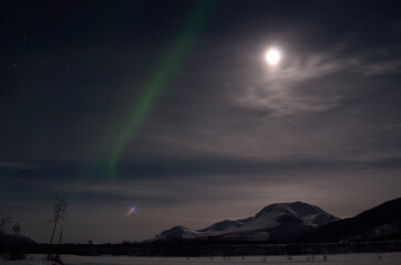 Naklejka na ściany i meble aurora borealis, northern light over snowy winter landscape with mountain and full moon at night
