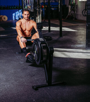 Strong sportsman using training machine in gym while pumping muscles during workout