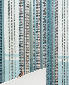 Relaxed female in white and dark striped dress sitting on concrete sloping roof and looking at camera in Hong Kong in China
