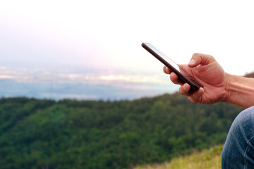 A man using a mobile phone during a summer adventure in the mountains. A male hand holds in his hand a smartphone and a mountain landscape in the background. Bulgaria. Balkans. Banner. Copy space.