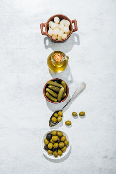 Top view of bowl with pickled cucumbers and plate with olives placed on table in row along with glass oil jug