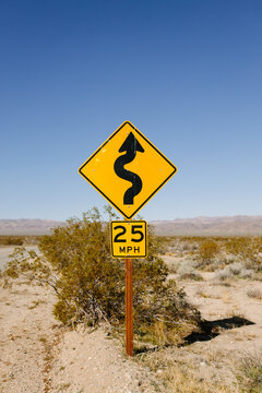 Yellow speed limit road sign locating in sandy area surrounded by dry grass in desert against clear summer sky in California