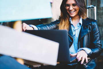 Cropped image of happy young woman in optical eyeglasses watching funny videos on digital laptop device sitting outdoors in cafe.Positive female having video chat with friend on modern computer