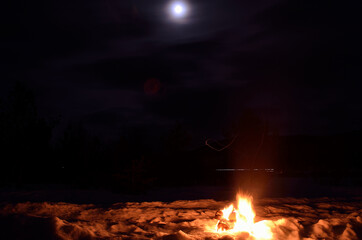 birch log fire on winter snow on a dark full moon night