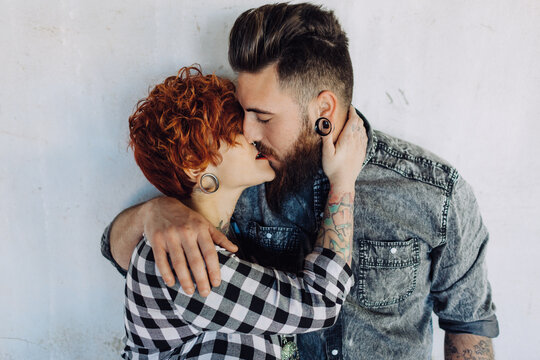 Positive young hipster couple with tattoos enjoying time together and hugging while standing against shabby stone construction in sunny day