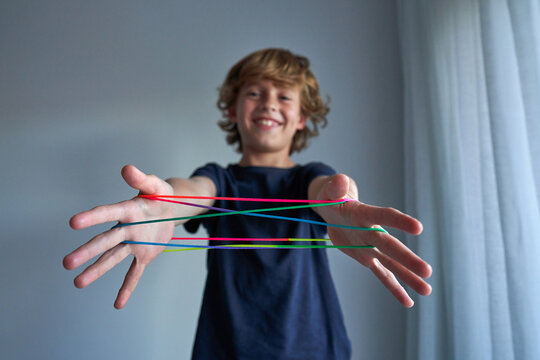 Excited schoolboy in pajamas creating difficult figure with string while playing cats cradle game at home
