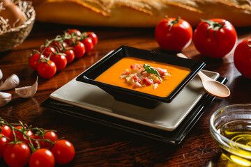 Receta típica española de salmorejo cordobés en un plato cuadrado y con algunos ingredientes al rededor.